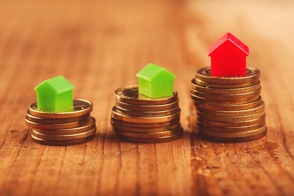 Small plastic house models on stacked coins illustrating the concept of value and price in a 1031 exchange with replacement property and the role of a qualified intermediary